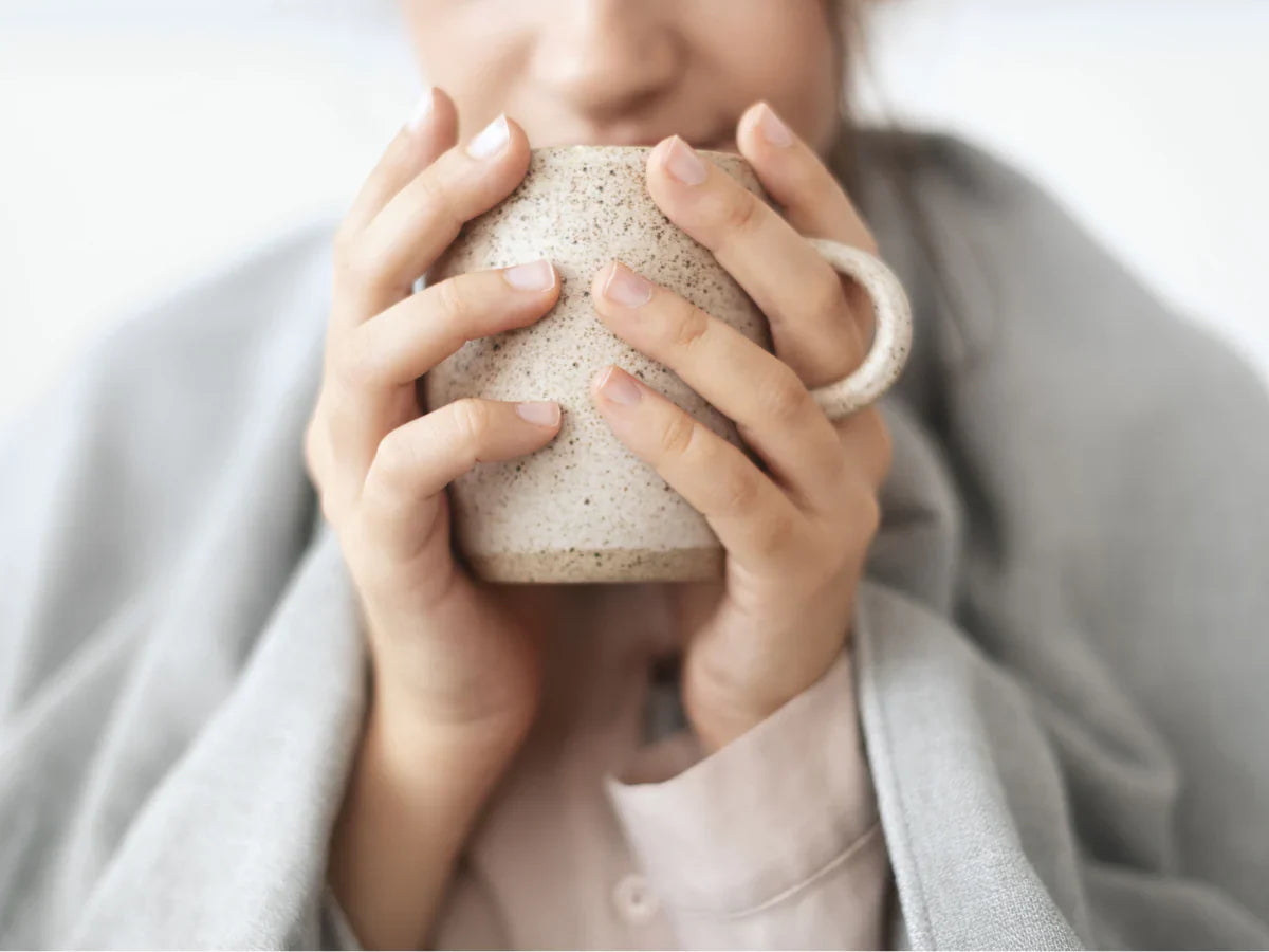 Femme qui se réchauffe avec une tasse, symbole d'immunité fragilisée en hiver et besoin de défenses naturelles